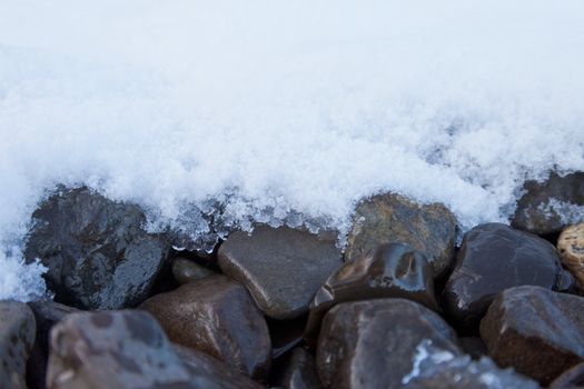 Winter nature background pattern abstract contrast of fresh snow thawing on wet coarse gravel rocks surface