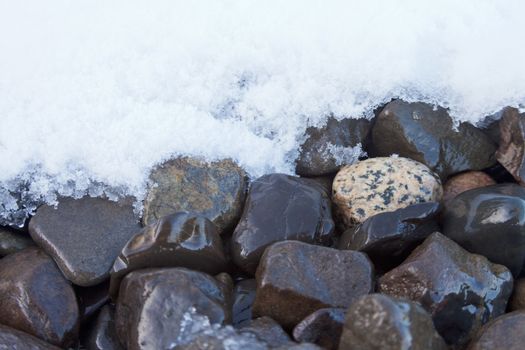 Winter nature background pattern abstract contrast of fresh snow melting on wet coarse gravel rocks surface