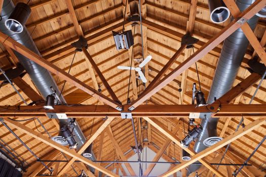 Heating vent ducts and light installation in timber house open wooden ceiling showing cross beam support structure and rafters