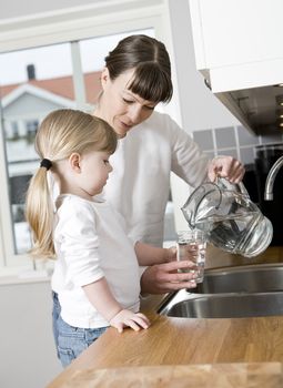 Small Girl in the kitchen with her mother drinking water