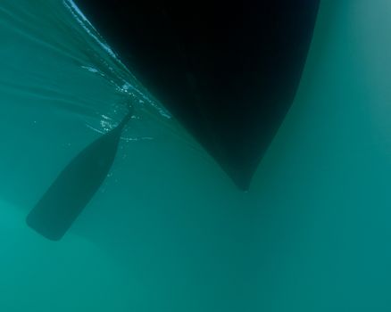 Dark body of canoe hull silhouette floating on water surface, paddle in the water, seen from underwater