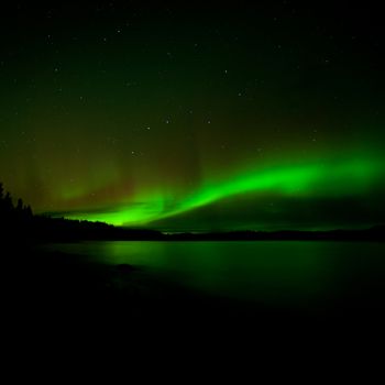 Band of aurora borealis or Northern Lights illuminates dark starry night sky over Lake Laberge, Yukon Territory, Canada