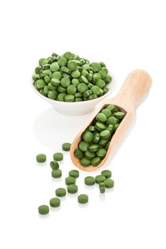 Green pills in bowl and on wooden scoop. Natural herbal alternative medicine. Chlorella, spirulina, wheat grass and barley grass. Healthy living.
