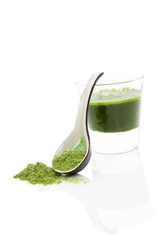 Green wheatgrass, spirulina and chlorella juice in glass isolated on white background with wheat grass powder on ceramic spoon. Healthy detox concept.