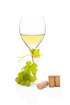 White wine in wine glass with green grapes, vine leaves and various wine corks isolated on white background. Luxurious wine still life.