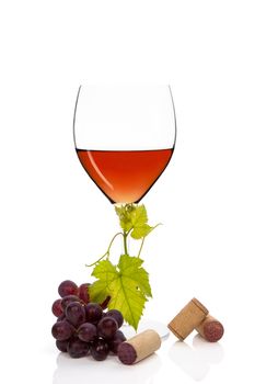 Luxurious rose wine in wine glass with red grapes, vine leaves and wine corks isolated on white background. Culinary exclusive wine.