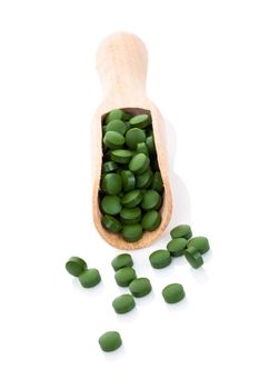 Green pills on wooden scoop isolated on white background with reflection. Spirulina, chlorella and wheatgrass. Healthy living concept.