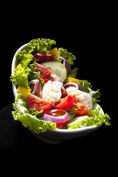 Luxurious fresh colorful vegetable salad in bowl isolated on black background. Culinary healthy eating.