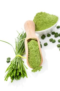 Natural herbal organic alternative medicine. Superfood. Wheatgrass powder, blades and green pills on wooden scoop and white bowl isolated on white. Healthy lifestyle.