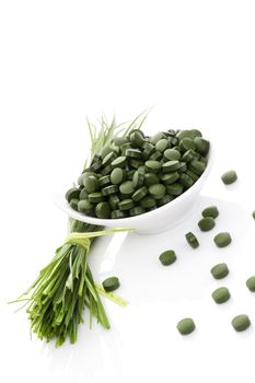 Wheatgrass blades and green spirulina pills isolated on white background. Healthy green eating. Vegan food supplement.