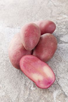 Red raw culinary potatoe isolated on natural stone background. Healthy vegetable eating. 