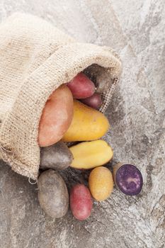 Various raw potatoes in brown bag on natural stone background. Healthy eating. Organic agriculture background.