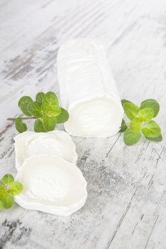 Goat cheese with fresh herbs on white wooden background. Luxurious traditional cheese still life, rustic style.