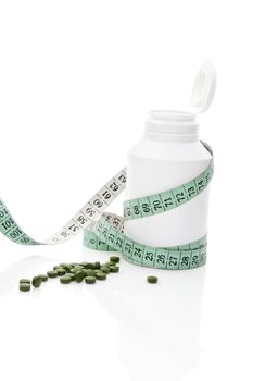 White pill bottle, measurement tape and green chlorella and spirulina pills isolated on white background. Natural healthy living. Detox a diet concept.