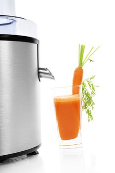Fresh carrot juice in glass and silver electric juicer isolated on white background with reflection. Healthy lifestyle, minimal sparse contemporary styles.