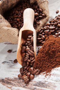 Coffee beans and ground coffee in brown sack on white wooden background. Gourmet coffee background, country style.