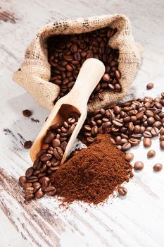 Coffee beans in sack and wooden spoon and ground coffee on white wooden background. Coffee background country style.