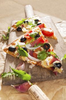 Pizza eating. Pizza piece with colorful toppings on wooden cutting board, with various ingredients, wine cork on brown background. Italian country style culinary kitchen.