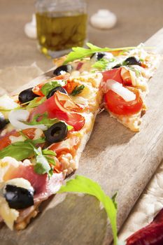 Culinary pizza eating. Pizza with prosciutto, ham, black olives, herbs on wooden cutting board on brown background. Traditional pizza background.