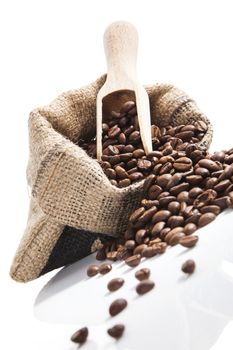 Fresh aromatic coffee beans in brown sack with wooden spoon isolated on white background. Culinary coffee drinking.