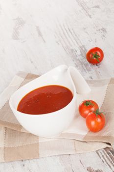 Delicious tomato soup with fresh tomatoes on white wooden textured background. Culinary soup appetizer.