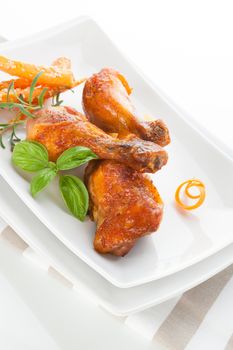 Delicious grilled chicken legs on white plate with fresh herbs and carrots isolated on white background. Culinary poultry eating.