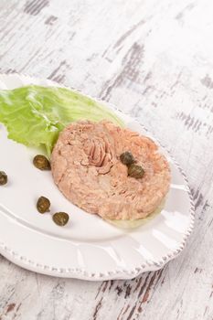 Tuna with capers and lettuce on vintage plate on white wooden textured background. Culinary seafood eating.