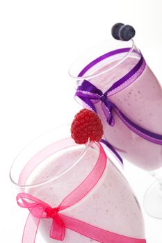 Raspberry and blueberry fruit milkshakes decorated with ribbon isolated on white background. Luxurious healthy summer drink.