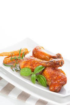 Chicken legs with fresh basil, rosemary and carrots on white plate. Culinary meat eating.