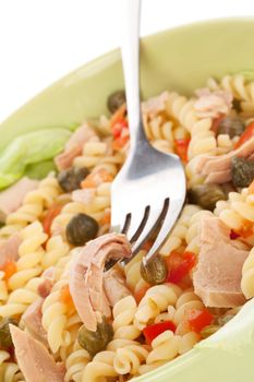 Delicious pasta with tuna, capers and vegetable in green bowl. Tuna piece on fork. Culinary eating.