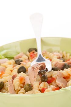 Tuna salad with tuna pieces, capers, and fusilli in green bowl. Tuna piece on fork. Culinary eating.