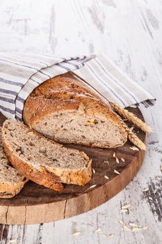 Whole grain baguette on round wooden kitchen board on white textured wooden background. Culinary bread eating, breakfast concept.