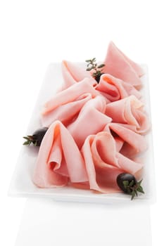 Delicious ham slices with black olives and fresh herbs isolated on white square. Culinary meat eating concept.