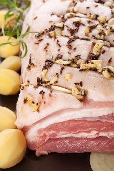 Pork belly background with fresh herbs, potatoes and onion on sheet pan ready to bake. Culinary meat eating.