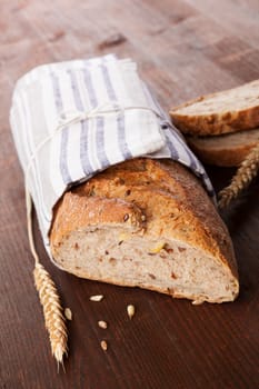 Brown whole grain baguette on dark brown wooden background. Delicious daily bread still life. Healthy eating.