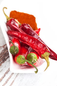 Dry and fresh chili peppers and paprika spice on white plate on white wooden textured background. Culinary cooking ingredients.