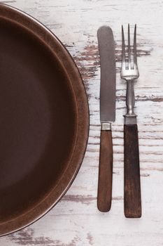 Empty plate with brown wooden cutlery on white wooden textured background, top view. Culinary gastronomy eating concept, rustic styles with copy space.