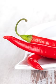 Fresh red hot chili peppers on white tray on white wooden textured background. Culinary cooking ingredients.