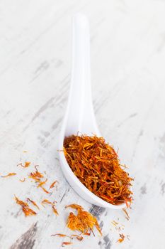 Luxurious saffron spice on white spoon on wooden textured background. Culinary spices.