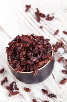 Full bowl of goji on white wooden textured background. Healthy traditional chinese eating supplement.