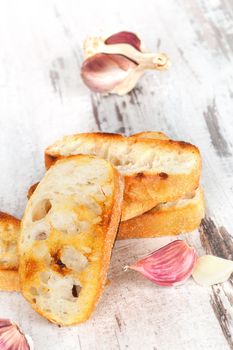 Garlic baguette with fresh garlic on white wooden textured background. Culinary eating, french country style.