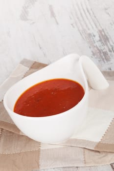 Delicious tomato soup in white bowl on white wooden textured background. Culinary italian soup eating. 