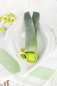 Delicious leek background. Raw leek on white plate on white wooden textured background. Healthy culinary veggie eating.