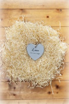 single wooden love heart in a love nest made of straw on floor boards