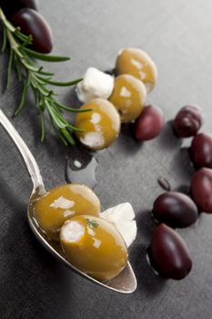 Luxurious green and black olive background. Olives on silver antique spoon, goat cheese and rosemary herb on dark grey and black background. Culinary greek and mediterranean eating. 