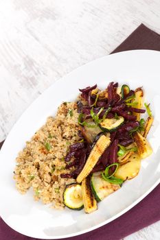 Couscous with fried vegetable on white plate on white wooden textured background. Culinary vegetarian eating.