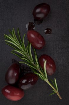 Delicious olive background. Black olives and fresh rosemary herb on black background, top view. Culinary eating.