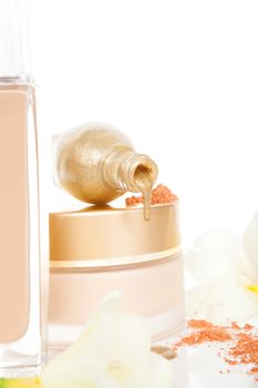 Luxurious cosmetics in beige and golden. Cream, makeup powder and golden nail polish with flower blossom isolated on white background.