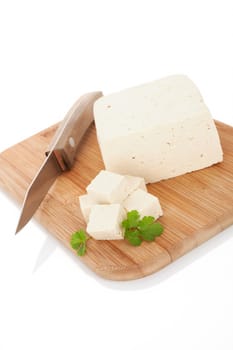 Tofu on wooden kitchen board with kitchen knife and fresh parsley. Culinary vegan and vegetarian eating.