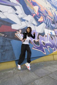 young attractive woman in hip hop dress dancing and jumping in urban background